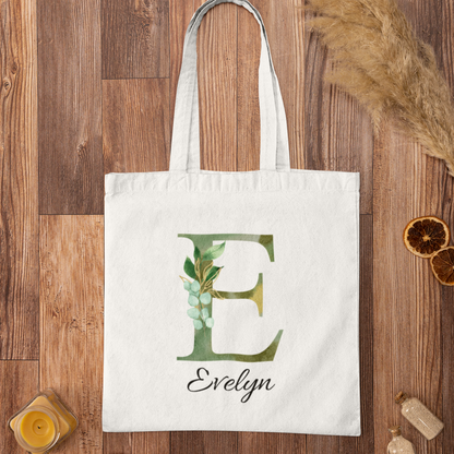 Botanical tote bag with letter E and name Evelyn on wooden surface, olive green foliage personalized gift