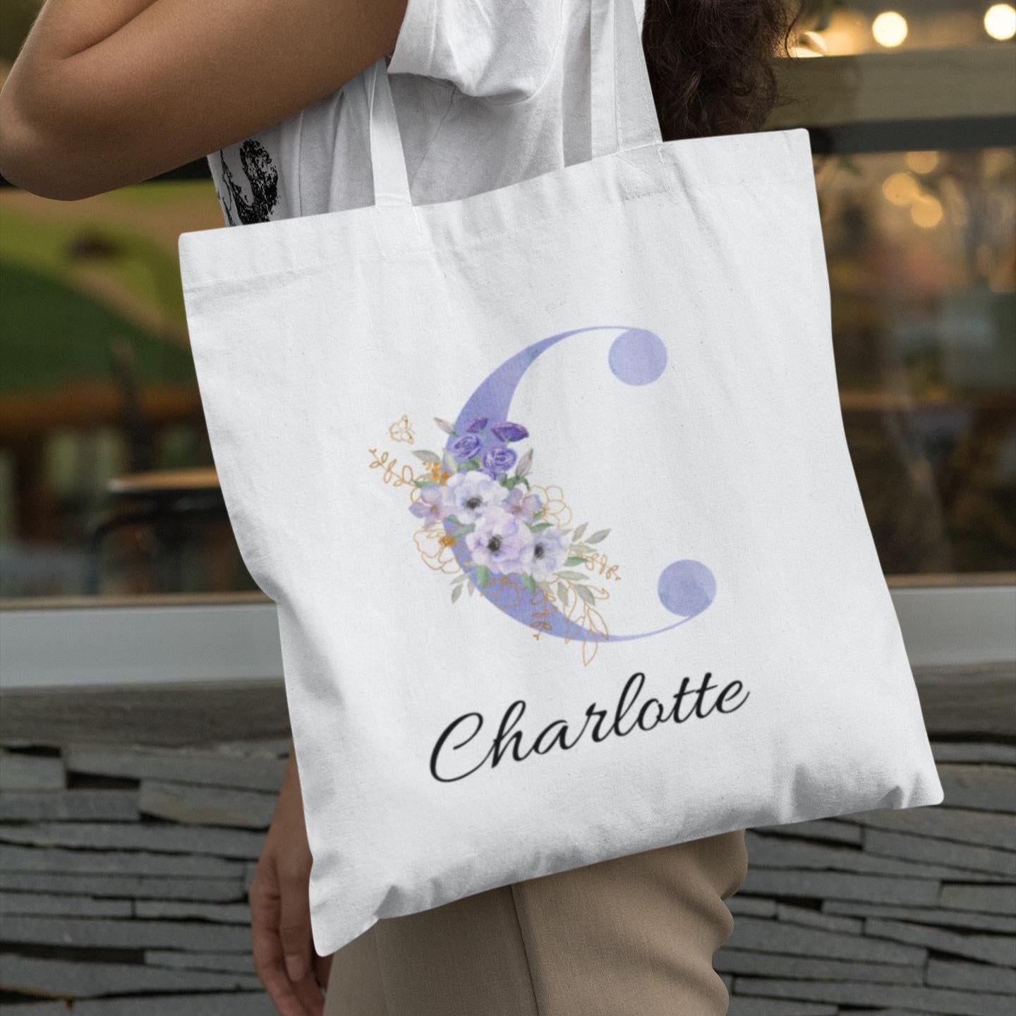 Woman carrying pastel purple and cornflower blue floral custom tote bag with initial letter C and name Charlotte, featuring elegant anemone flower artwork