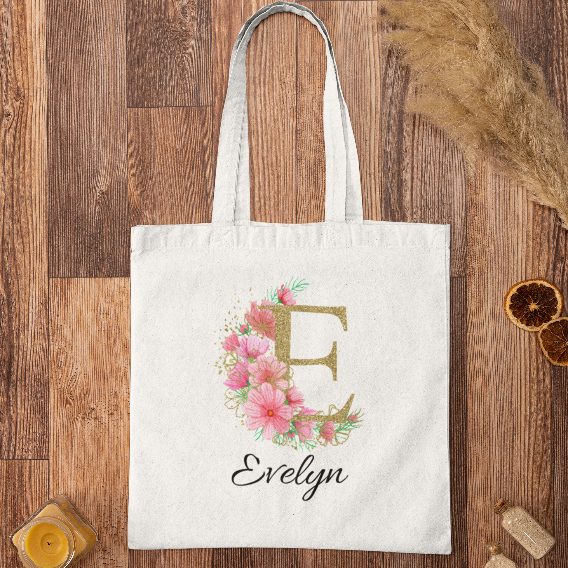 Elegant pink and gold floral initial tote bag with letter E and name Evelyn, flat lay on wooden surface
