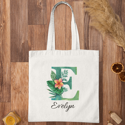 Plumeria Tropical Floral Custom Tote Bag with Emerald Green Initial E, personalized name Evelyn, flatlay on wooden background