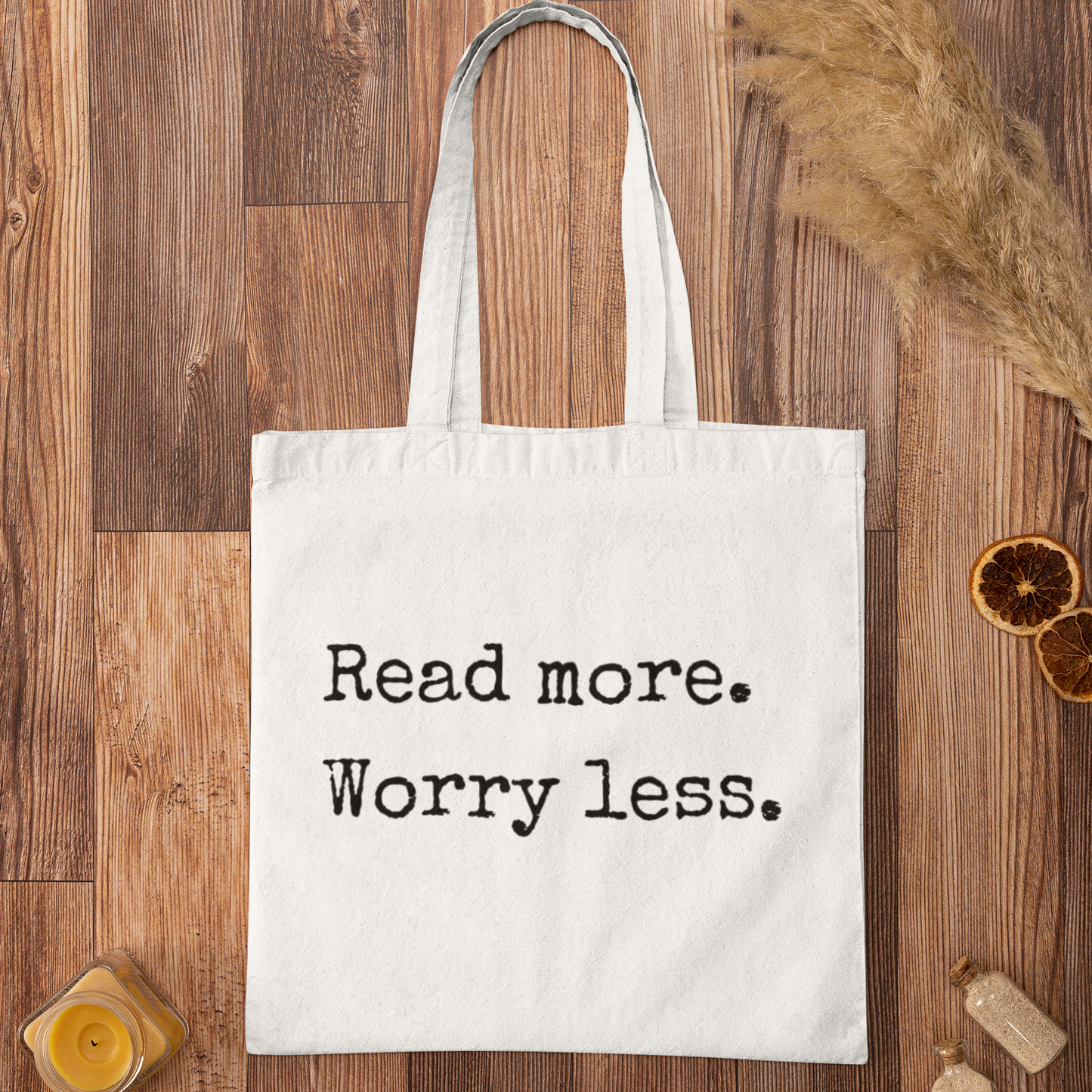 White cotton book tote bag with ‘Read more. Worry less.’ quote on wooden background – minimalist design