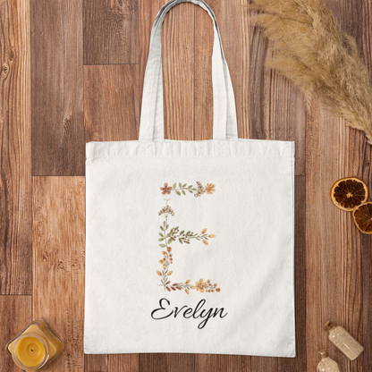 Rustic floral tote bag with letter E and name Evelyn on wooden surface, custom name canvas bag